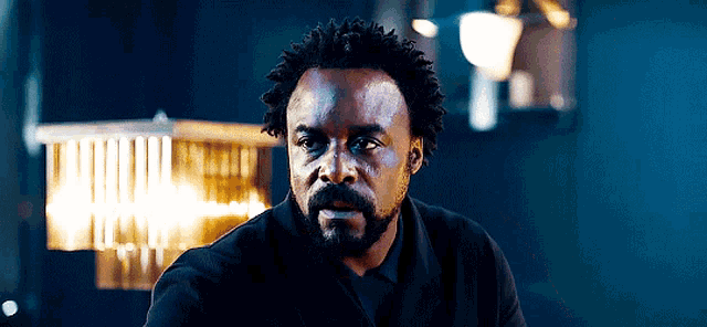 a man with curly hair and a beard is sitting in a dark room