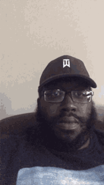 a man wearing glasses and a baseball cap with the letter t on it