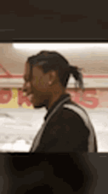 a man with his hair in a ponytail is standing in front of a store .