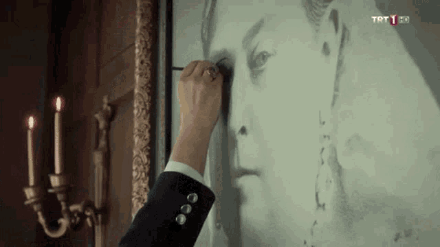 a man in a suit is drawing a picture of a woman 's face on a wall with candles in the background