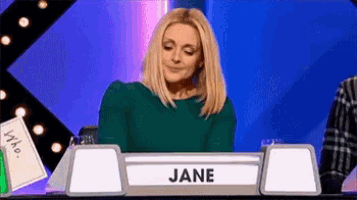 a woman in a green sweater is sitting at a table with a sign that says jane .