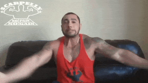 a man in a red tank top sitting on a couch with his arms outstretched
