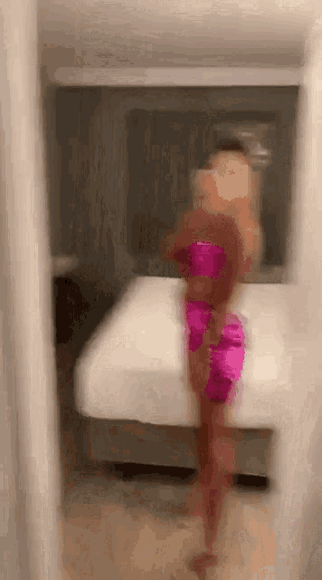 a blurry picture of a woman in a pink dress standing in front of a bed in a room .