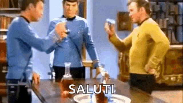 three men are standing around a table with a bottle of whiskey and the word saluti written on the table .