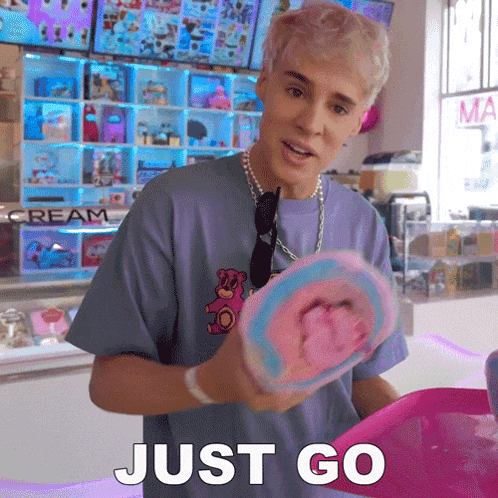 a man in a purple shirt is holding a piece of cotton candy and the word just go is on the bottom right