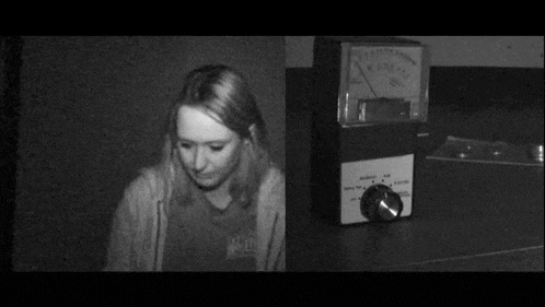 a black and white photo of a woman standing in front of a meter that says ' voltage ' on it .