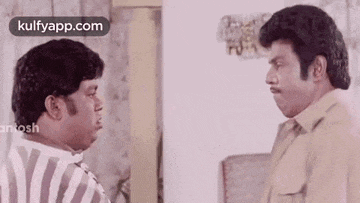two men are standing next to each other and talking to each other in a living room .