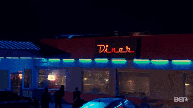a diner is lit up at night with a car parked in front of it
