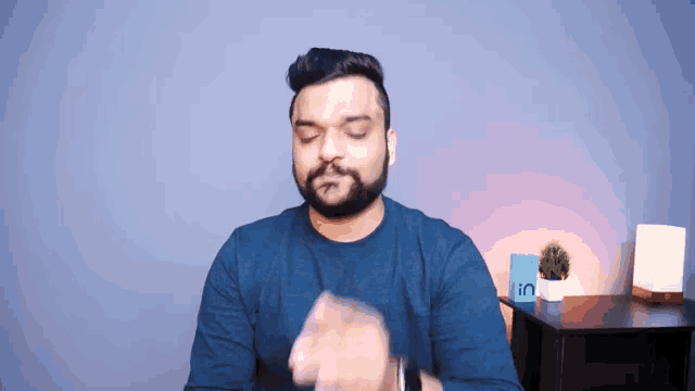a man with a beard wearing a blue shirt is standing in front of a table with the word in on it