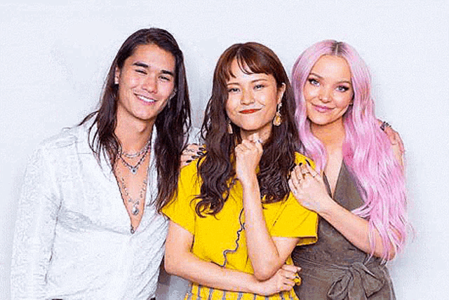 a man with long hair and two women with pink hair are posing for a picture together .