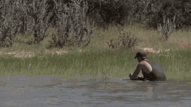 a man in a tank top is walking through a muddy stream .