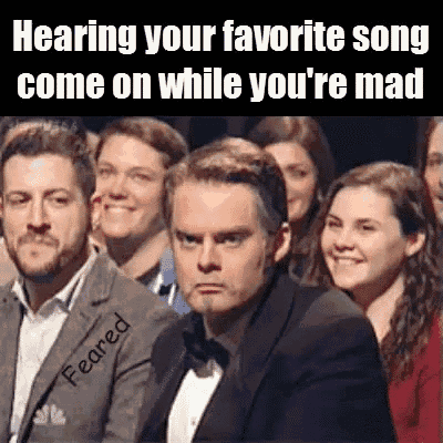 a man in a tuxedo is sitting in front of a crowd of people and making a funny face .