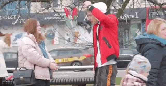 a man in a red jacket is standing next to a woman in a pink jacket on a city street .