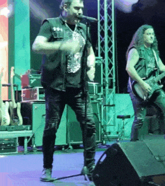 a man sings into a microphone while another man plays guitar
