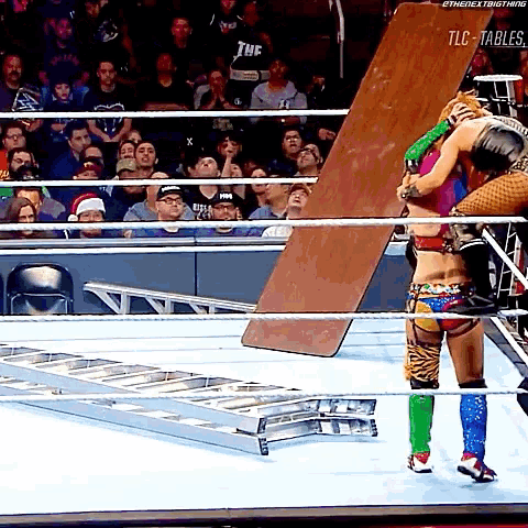 a woman in a wrestling ring holds a large piece of wood in her hands