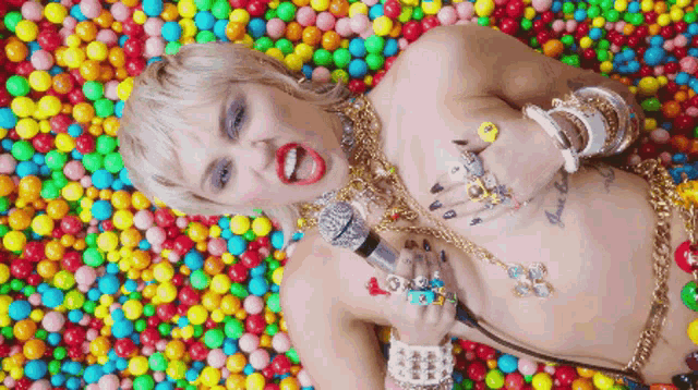 a naked woman is laying on a pile of candy balls holding a microphone .
