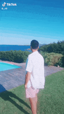 a man in a white shirt and pink shorts is standing in front of a swimming pool and looking at the ocean