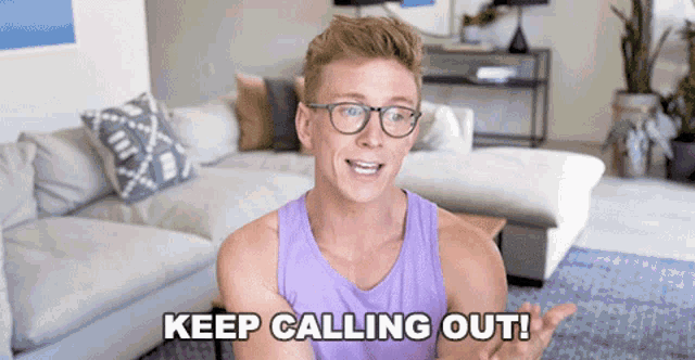 a man wearing glasses says keep calling out in front of a couch