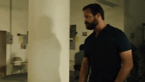 a man with a beard is standing in a room next to a white wall .