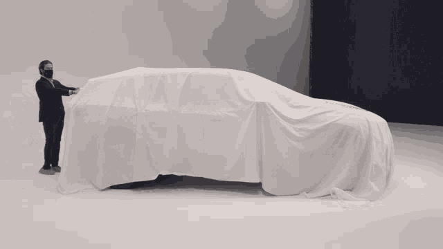 a man in a suit covering a car with a white cloth