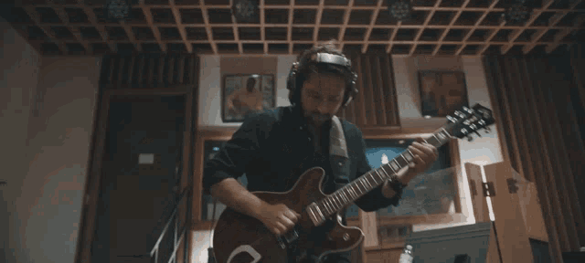 a man wearing headphones plays a guitar in a room
