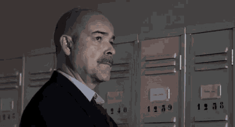 a man in a suit is standing in front of a row of lockers with the numbers 123456789 on them .