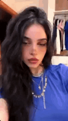 a woman with long black hair is wearing a blue shirt and necklace .