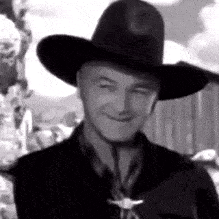 a man is wearing a cowboy hat and smiling in a black and white photo .