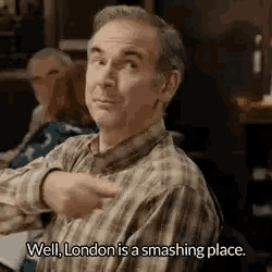 a man in a plaid shirt is pointing at something while sitting at a table .
