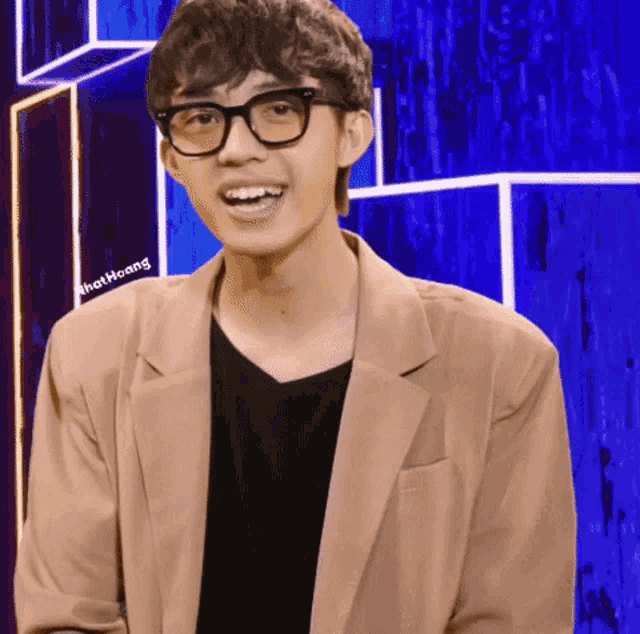 a young man wearing glasses and a tan jacket has that hoang written on the bottom of his chest