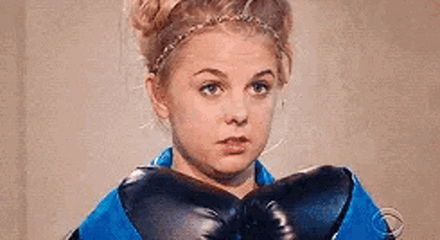 a young woman wearing boxing gloves and a blue jacket is making a funny face .