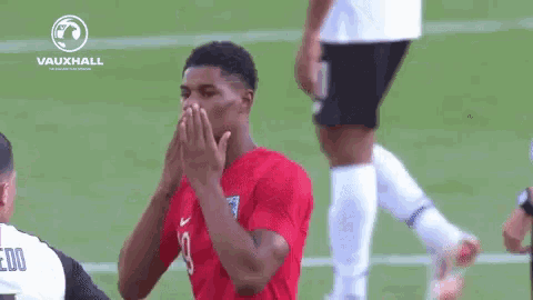 a soccer player is covering his face with his hands while standing on a soccer field .