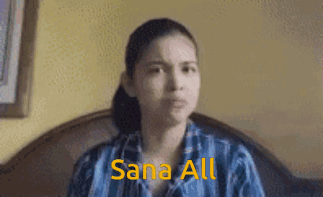 a woman in a blue shirt is sitting on a bed with the words sana all written above her .