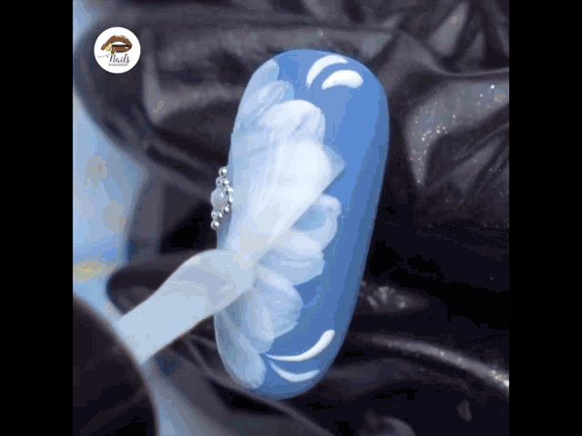 a close up of a blue nail with a white flower design on it