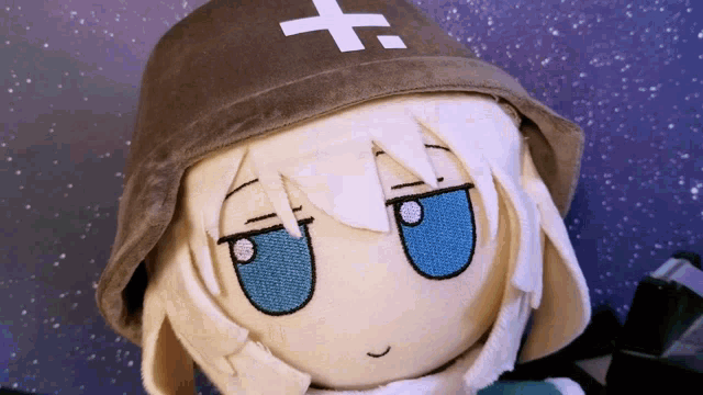 a stuffed doll with white hair and blue eyes has a hat with a cross on it