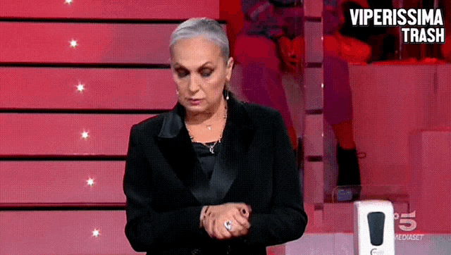 a woman in a black suit is standing in front of a red wall with the words viperissima trash on it
