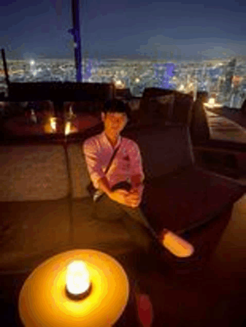 a man is sitting on a couch in a dark room with a candle in the foreground .