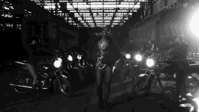 a black and white photo of a woman standing next to motorcycles