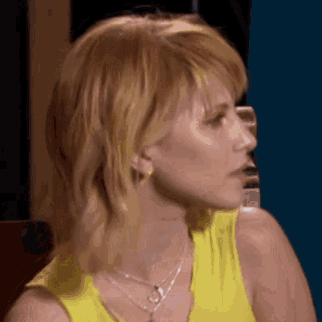 a woman in a yellow tank top and necklace is looking to the side .