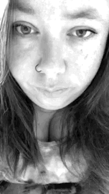a black and white photo of a young woman 's face with a nose ring .
