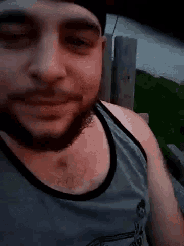 a man with a beard is wearing a tank top and hat .