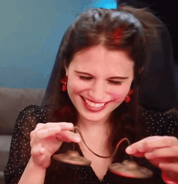 a woman in a black polka dot shirt is smiling while holding a pair of bells