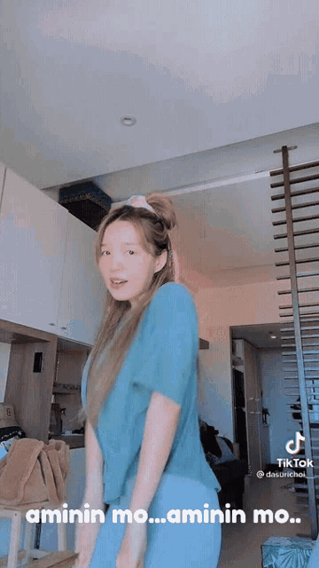 a woman in a blue shirt is dancing in a room with the words aminin mo.. aminin mo.. on the bottom