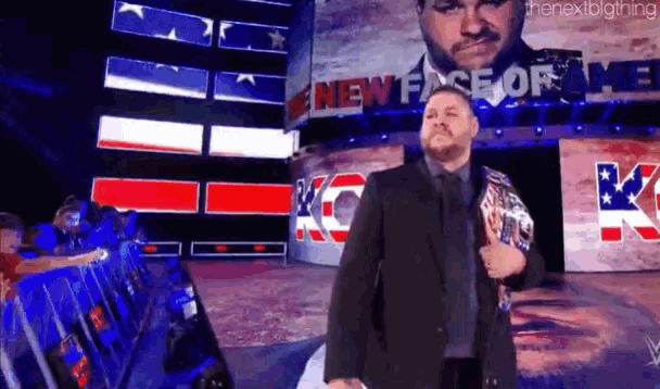 a man in a suit and tie is walking on a stage holding a wrestling championship belt .