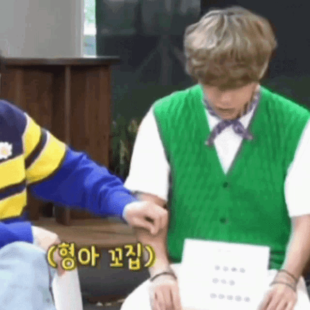a man in a green vest is sitting next to a man in a yellow and blue sweater .