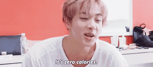 a young man in a white shirt is sitting in front of a red wall and says `` it 's zero calories . ''