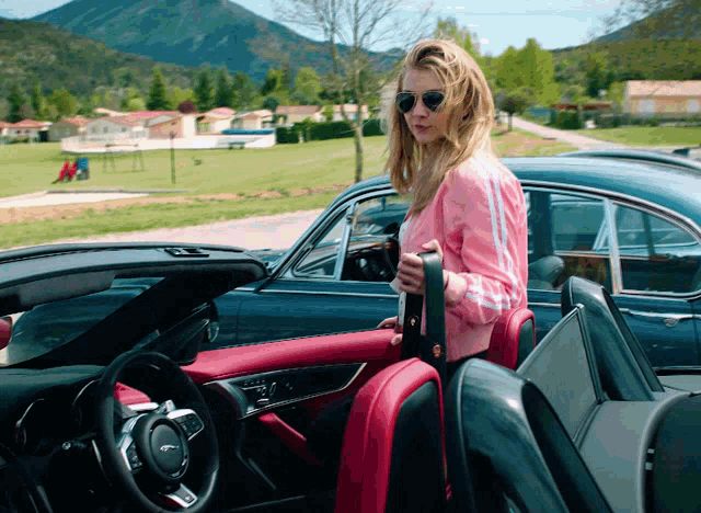 a woman in a pink jacket is getting out of a blue car