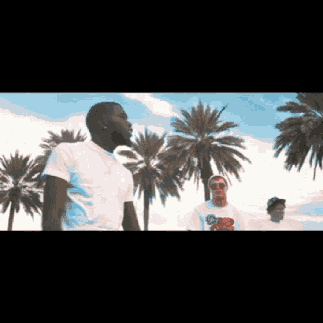 three men standing in front of palm trees in a video