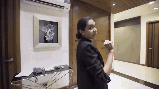 a woman in a black jacket is standing in a hallway with a picture on the wall