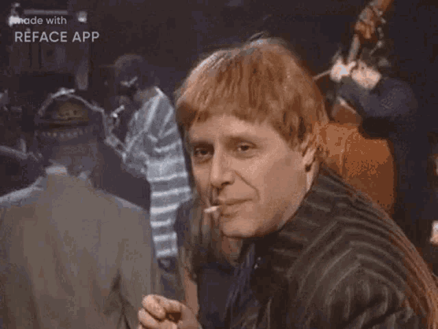 a man with red hair is giving the ok sign while sitting in front of a group of people .
